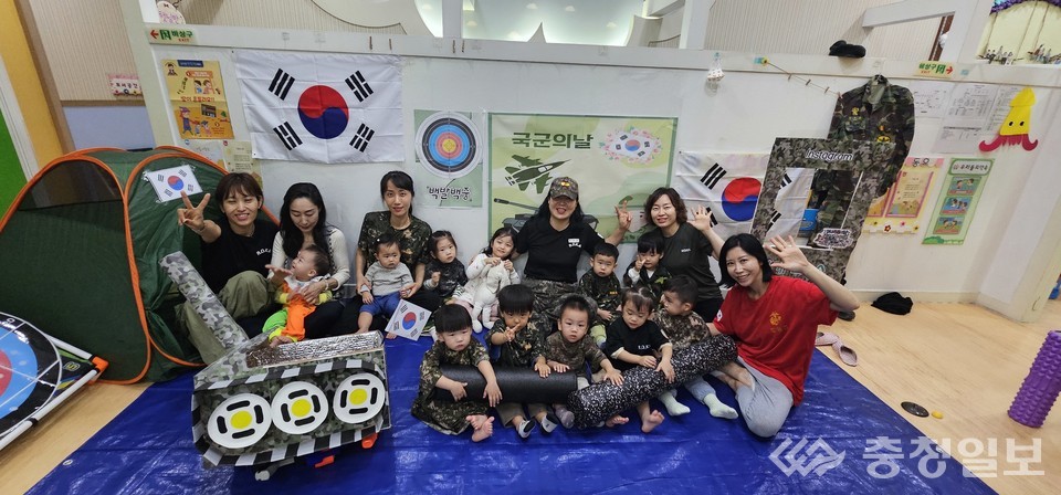 ▲ 국군의 날을 기념해 스마트시티 어린이집 원생들과 교사들이 군복과 태극기 소품을 활용해 단체사진을 찍는 모습. 작은 장난감 전차와 캠프장 분위기를 연출한 배경 속에서 아이들은 밝은 표정으로 포즈를 취하고 있으며, 교사들도 함께 손을 흔들며 즐거운 분위기를 더하고 있다
