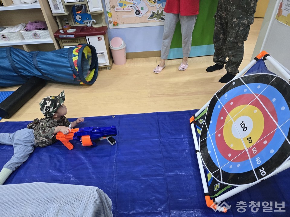 ▲ 파란 매트 위에서 엎드린 자세로 집중하는 아이의 모습이 마치 작은 군인을 연상케 하며, 주변 교사들이 지켜보며 따뜻한 미소로 격려하고 있다
