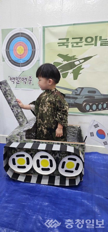 ▲ 군복을 입은 아이가 탱크에 올라서 즐겁게 체험 활동을 하고 있는 모습. 옆에는 태극기와 과녁판, ‘국군의 날’ 포스터가 함께 전시돼 있어 행사의 분위기를 더욱 생생하게 보여준다