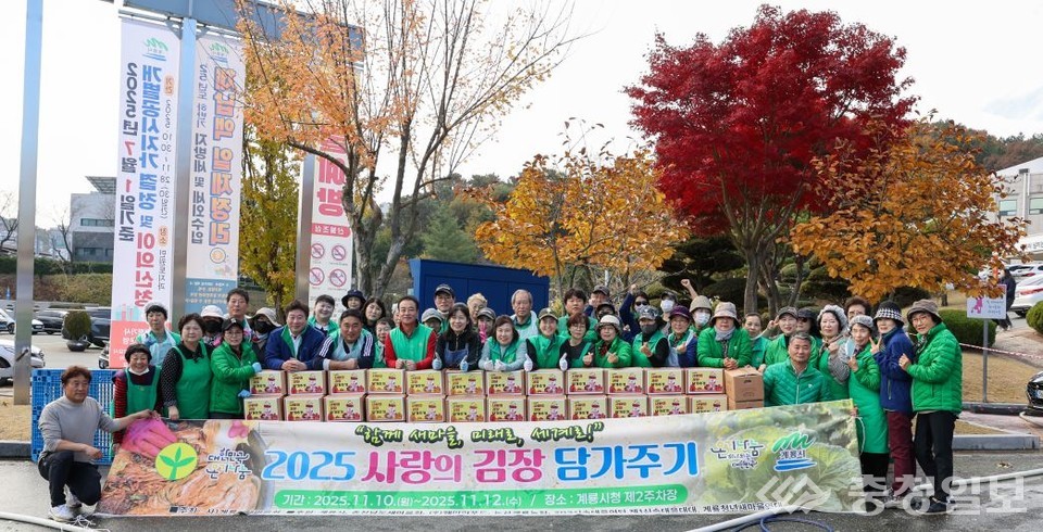 ▲ 계룡시새마을회 회원들과 지역 봉사자들이 함께한 ‘2025 사랑의 김장 담가주기’ 행사 현장. 정성스럽게 마련한 김장 꾸러미가 테이블 위에 가득 쌓여 있으며, 참여자들이 환한 표정으로 이웃에게 따뜻한 마음이 전해지길 바라는 마음을 전하고 있다. 만추의 단풍이 물든 시청 앞 풍경이 행사 분위기를 더욱 따뜻하게 물들인다