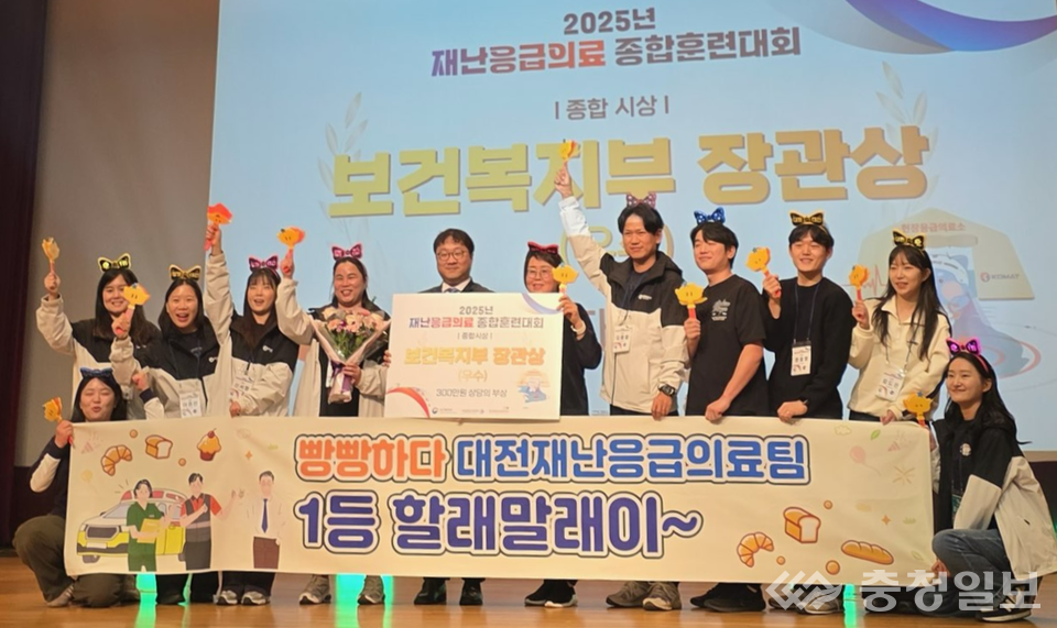 ▲ 대전 재난응급의료팀이 ‘2025년 재난응급의료 종합훈련대회’에서 보건복지부 장관상(우수상)을 수상한 뒤 무대에서 기념 촬영하고 있다. 팀원들이 손팻말과 머리띠를 착용해 밝은 분위기 속에서 성과를 함께 축하하고 있다.