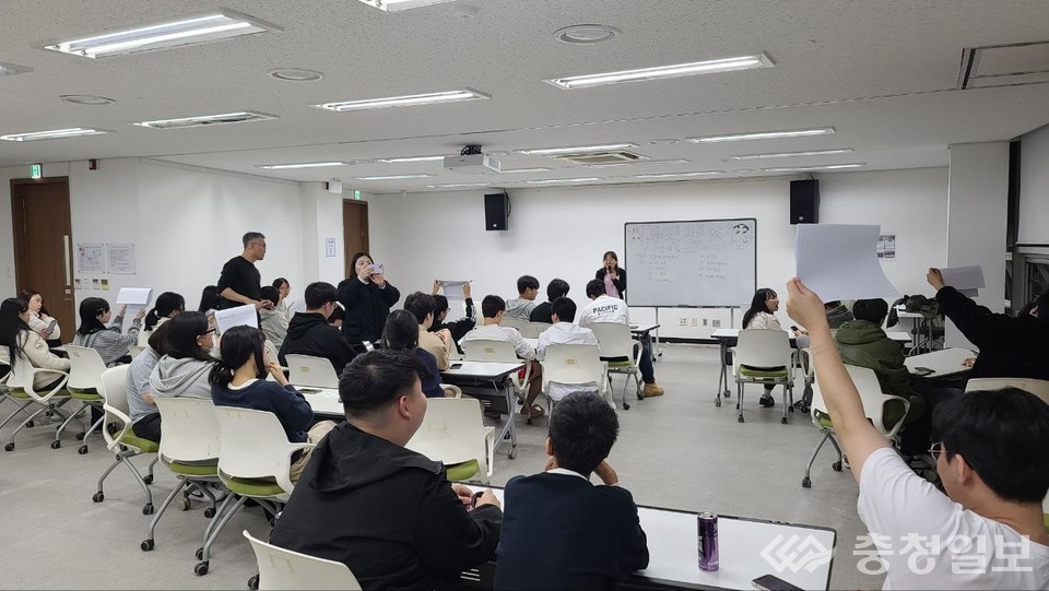 ▲ 강의실에서 학생들이 테이블에 둘러앉아 참여형 수업을 진행하는 모습. 한 학생이 손을 들어 결과물을 발표하고, 교사가 앞에서 설명을 이어가며 서로의 의견을 공유하는 역동적 학습 장면이 포착됐다