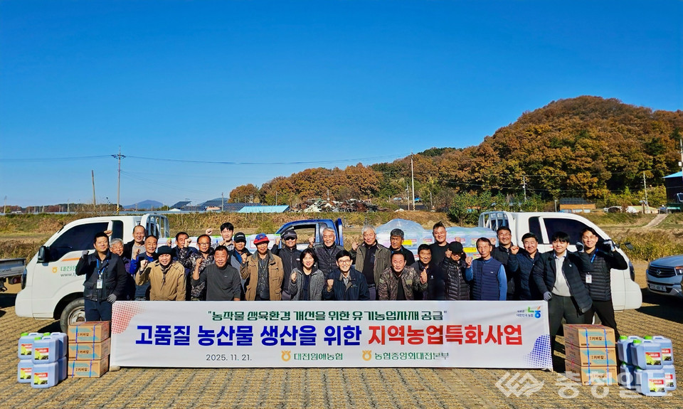 ▲ 대전원예농협이 유기농업자재를 농가에 전달하는 자리에서 농업인들과 관계자들이 함께 모여 지원 사업의 취지를 공유하며 기념 모습을 연출하고 있다. 배경에는 농경지와 가을 산세가 펼쳐져 있어 현장감을 더한다